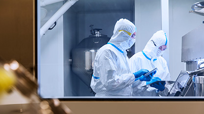 Scientists in cleanroom suits using digital tablets during a laboratory experiment