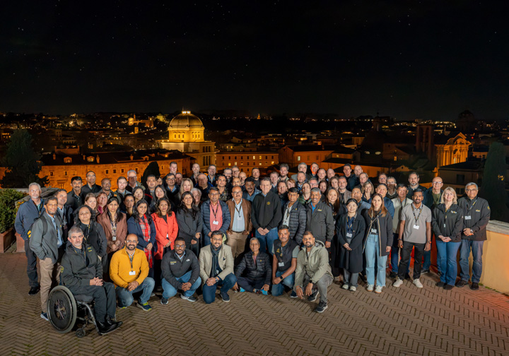 A large group of Intertek colleagues poses for a picture on top of a building in Rome at night. 
